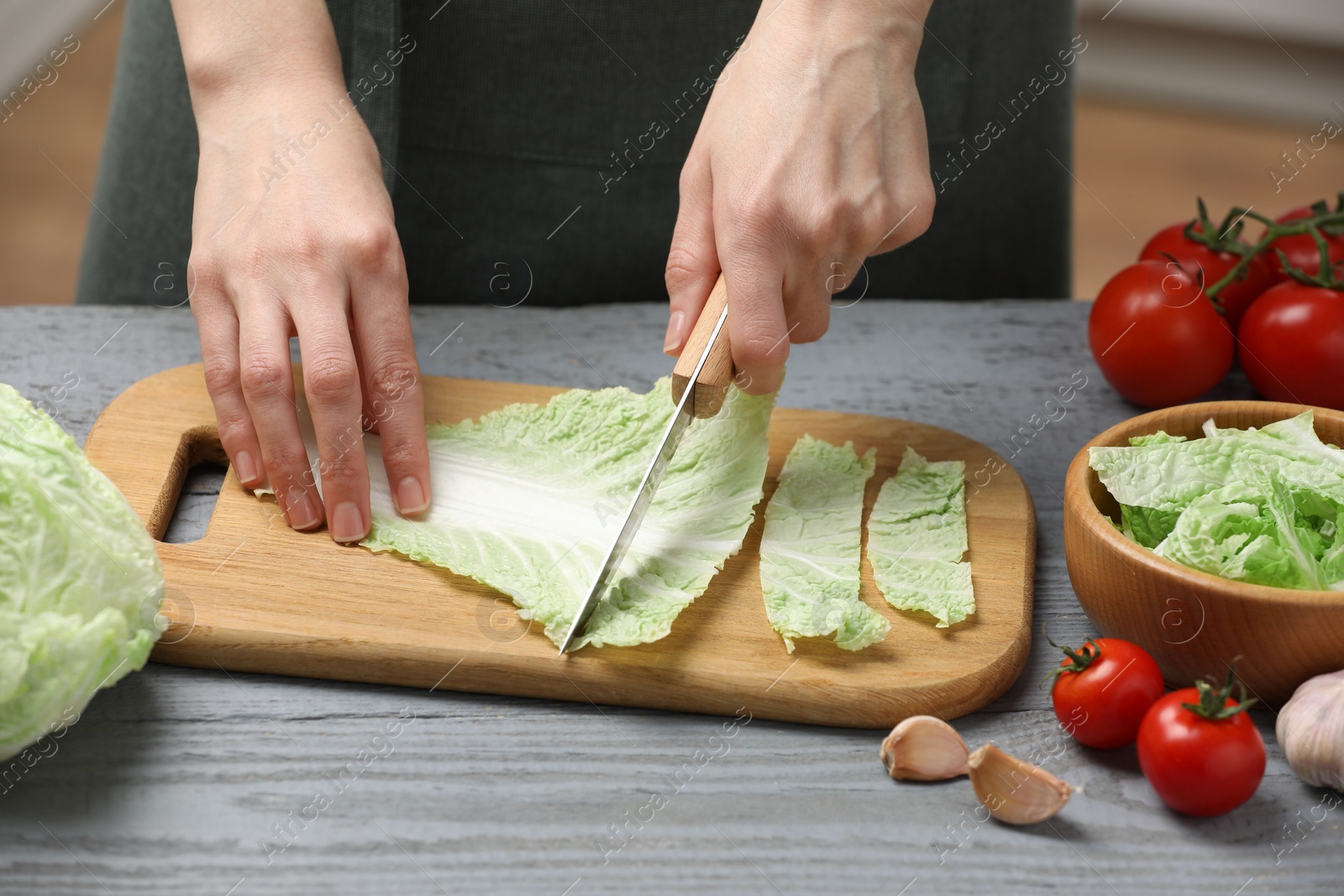 Photo of Woman cutting leaf of fresh chinese cabbage at grey wooden table in kitchen, closeup