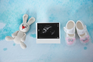 Photo of Ultrasound photo, baby shoes and toy on color background, top view