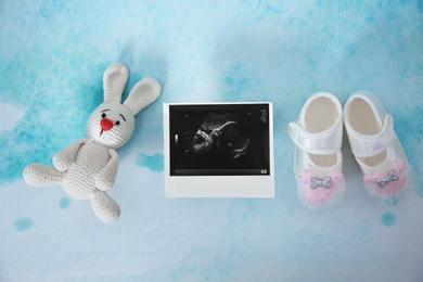 Ultrasound photo, baby shoes and toy on color background, top view