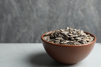Photo of Raw sunflower seeds in bowl on grey table. Space for text