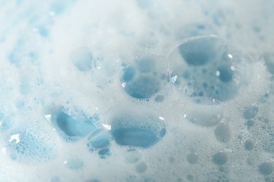 Photo of Foam on light blue background, closeup. Face cleanser, skin care cosmetic