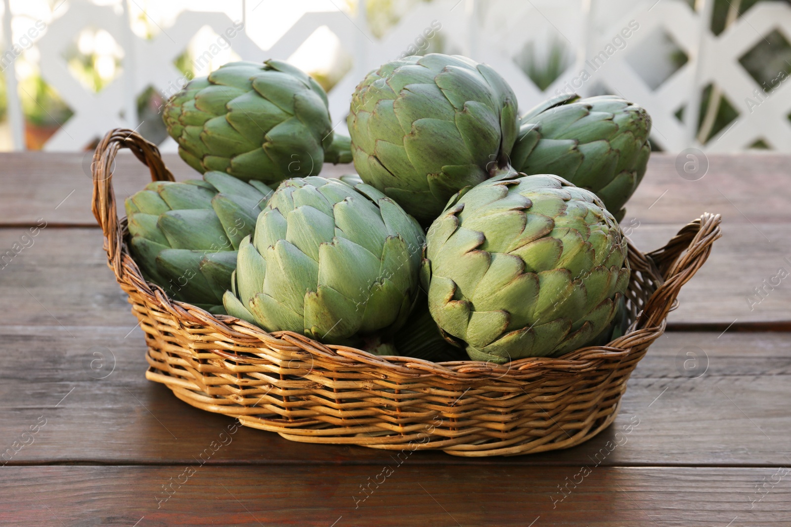 Photo of Wicker basket with fresh raw artichokes on wooden table
