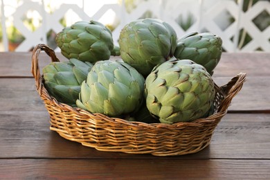 Wicker basket with fresh raw artichokes on wooden table