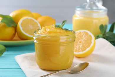 Photo of Delicious lemon curd in glass jar, fresh citrus fruits, mint and spoon on light blue wooden table