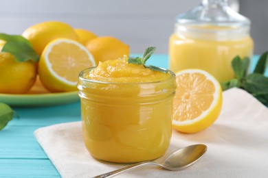 Delicious lemon curd in glass jar, fresh citrus fruits, mint and spoon on light blue wooden table