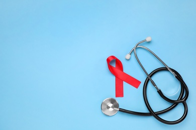 Photo of Red ribbon and stethoscope on light blue background, flat lay with space for text. AIDS disease awareness