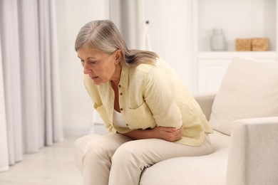 Photo of Menopause. Woman suffering from abdominal pain on sofa at home