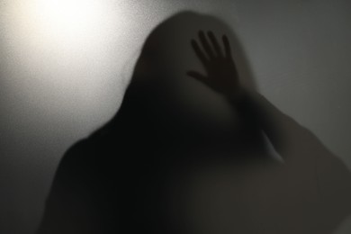 Photo of Silhouette of ghost behind glass against light grey background