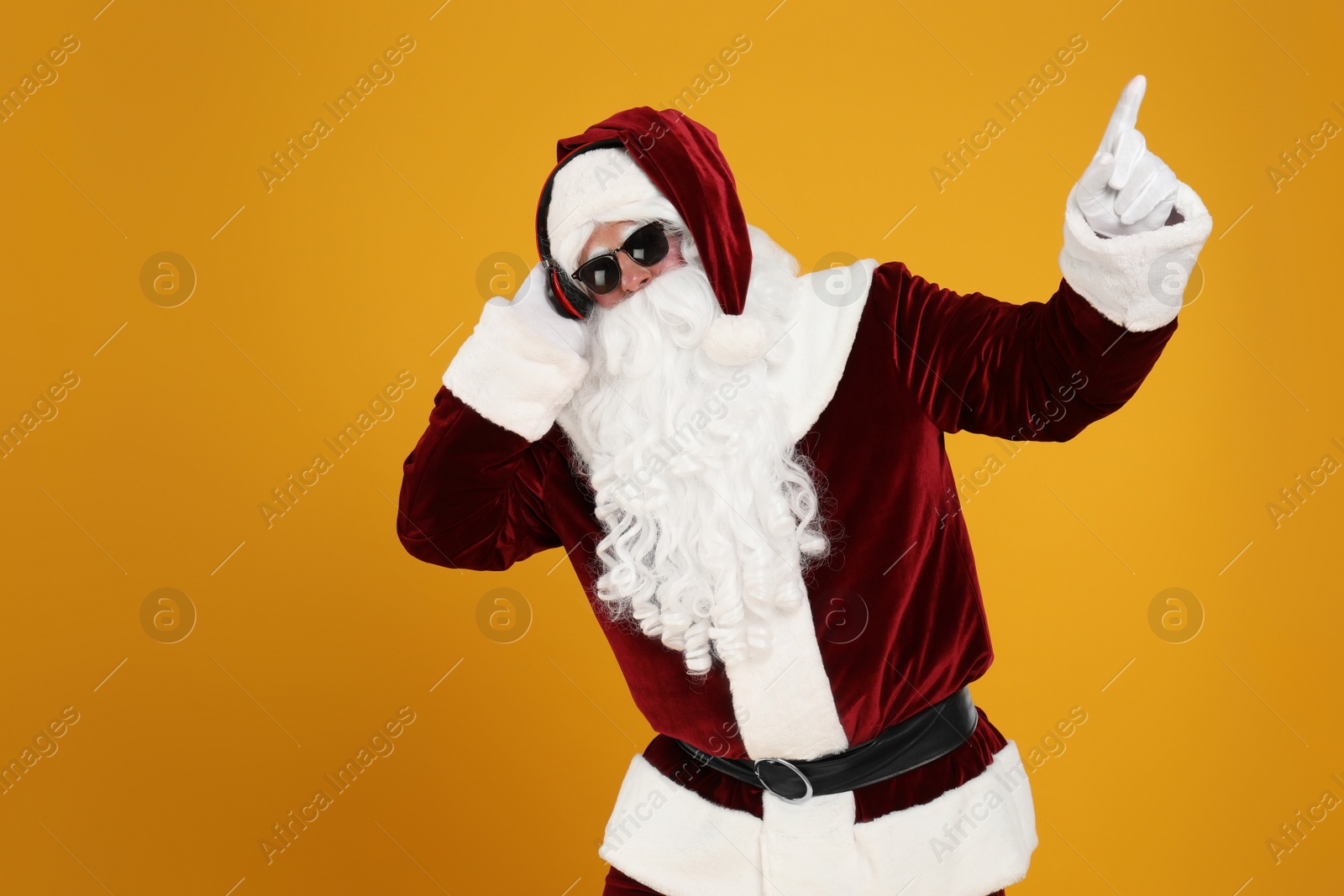 Photo of Santa Claus with headphones listening to Christmas music on yellow background