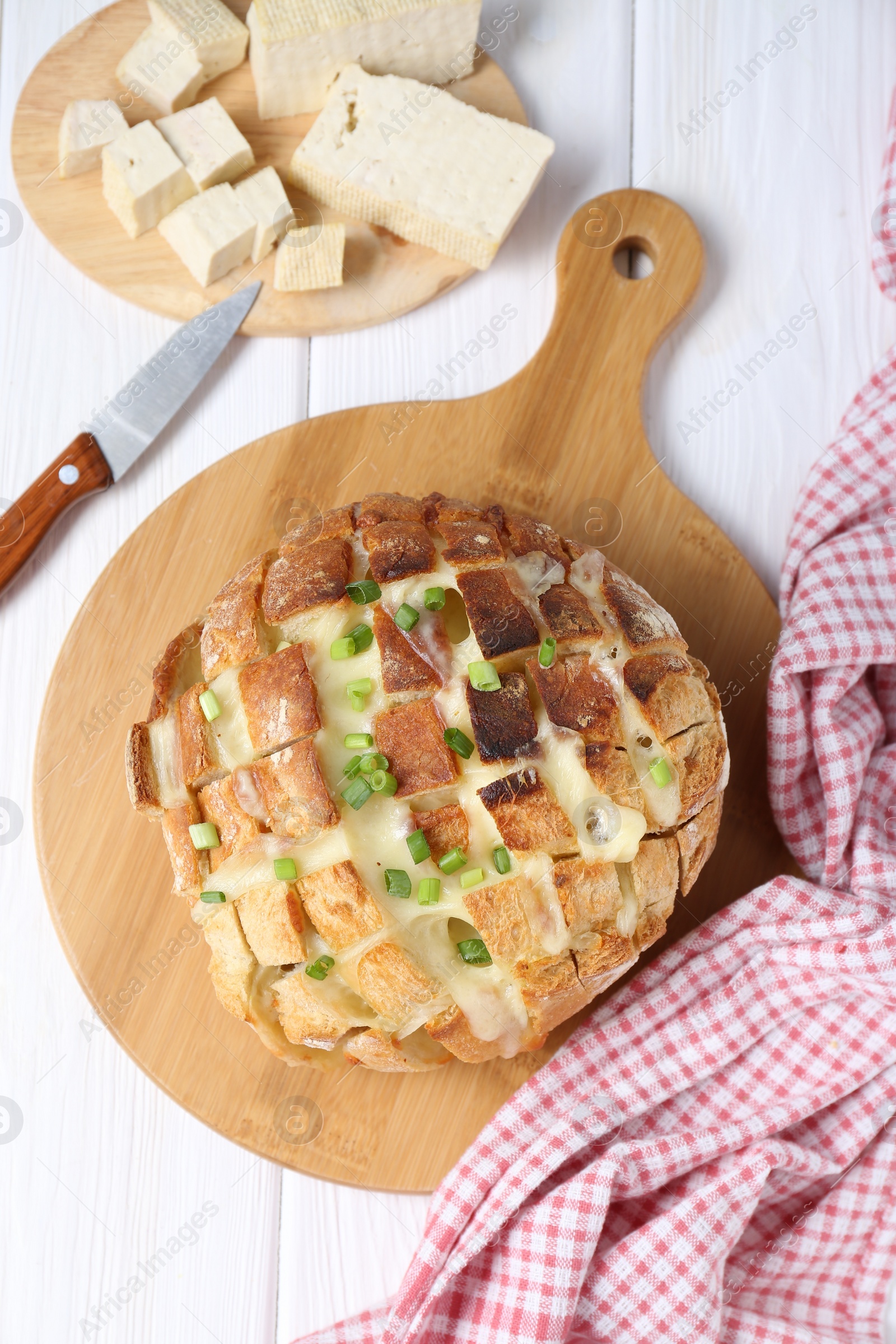 Photo of Freshly baked bread with tofu cheese, green onions and knife on white wooden table, flat lay