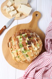 Freshly baked bread with tofu cheese, green onions and knife on white wooden table, flat lay