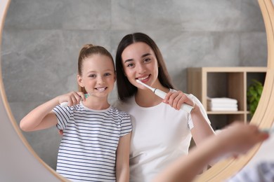 Mother and her daughter brushing teeth together near mirror in bathroom