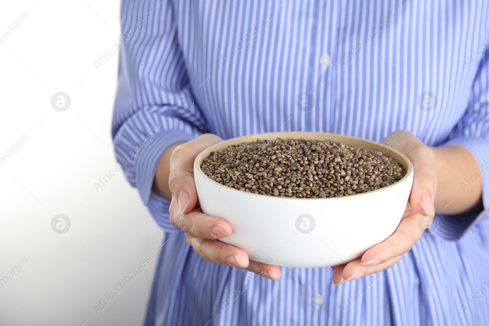 Photo of Woman holding bowl with hemp seeds on white background, closeup