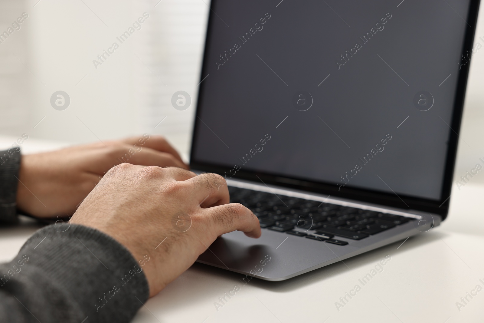 Photo of E-learning. Young man using laptop at white table, closeup