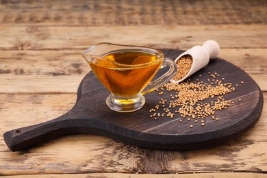 Photo of Jug of natural oil and mustard seeds on wooden table