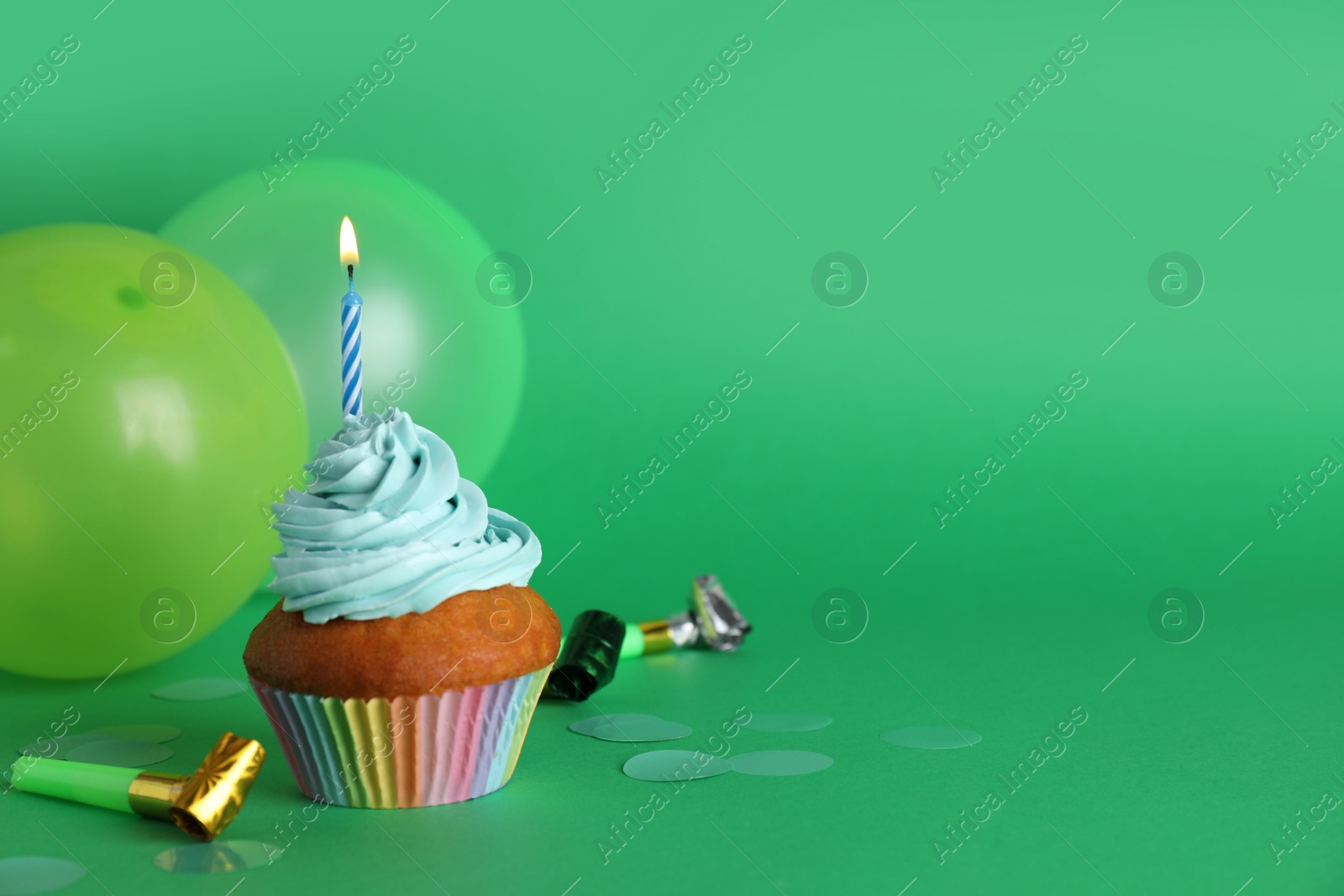 Photo of Delicious birthday cupcake with candle near balloons and party blowers on green background, space for text