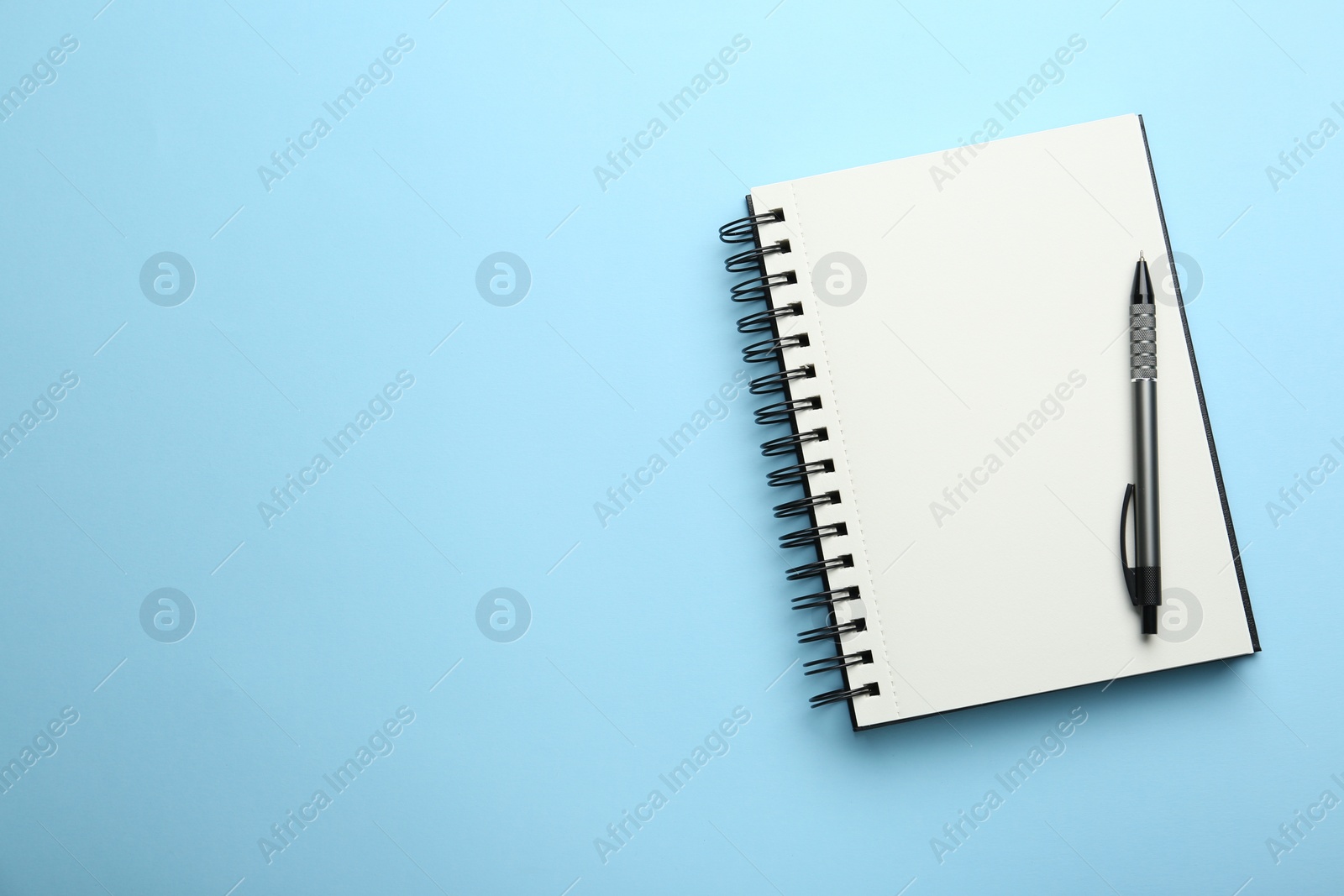 Photo of Notebook and pen on light blue background, top view. Space for text