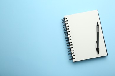 Notebook and pen on light blue background, top view. Space for text