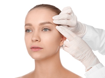 Doctor examining young woman face before cosmetic surgery on white background