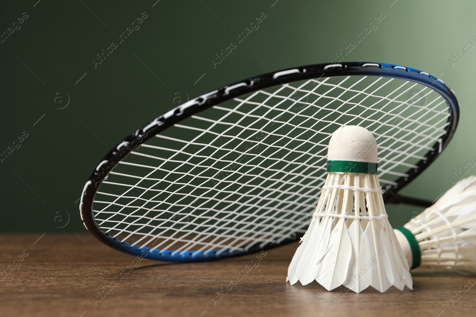 Photo of Feather badminton shuttlecocks and racket on wooden table against green background, closeup. Space for text