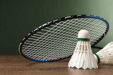 Photo of Feather badminton shuttlecocks and racket on wooden table against green background, closeup. Space for text