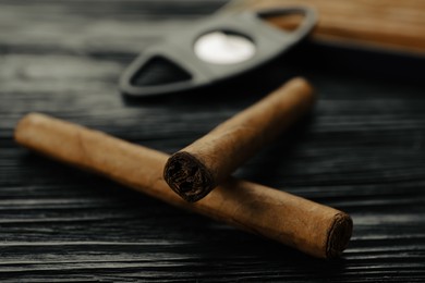 Photo of Cigars wrapped in tobacco leaves on black wooden table, closeup