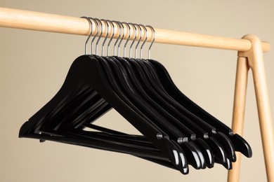 Photo of Black clothes hangers on wooden rack against beige background, closeup view