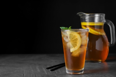 Photo of Delicious iced tea on grey table against black background, space for text