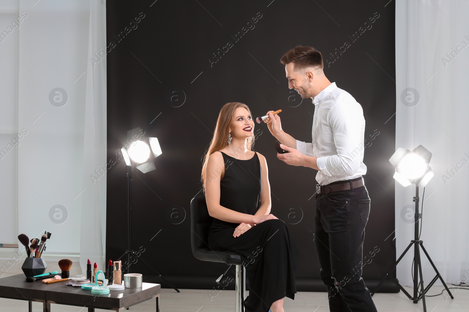 Photo of Professional makeup artist working with beautiful young woman in photo studio