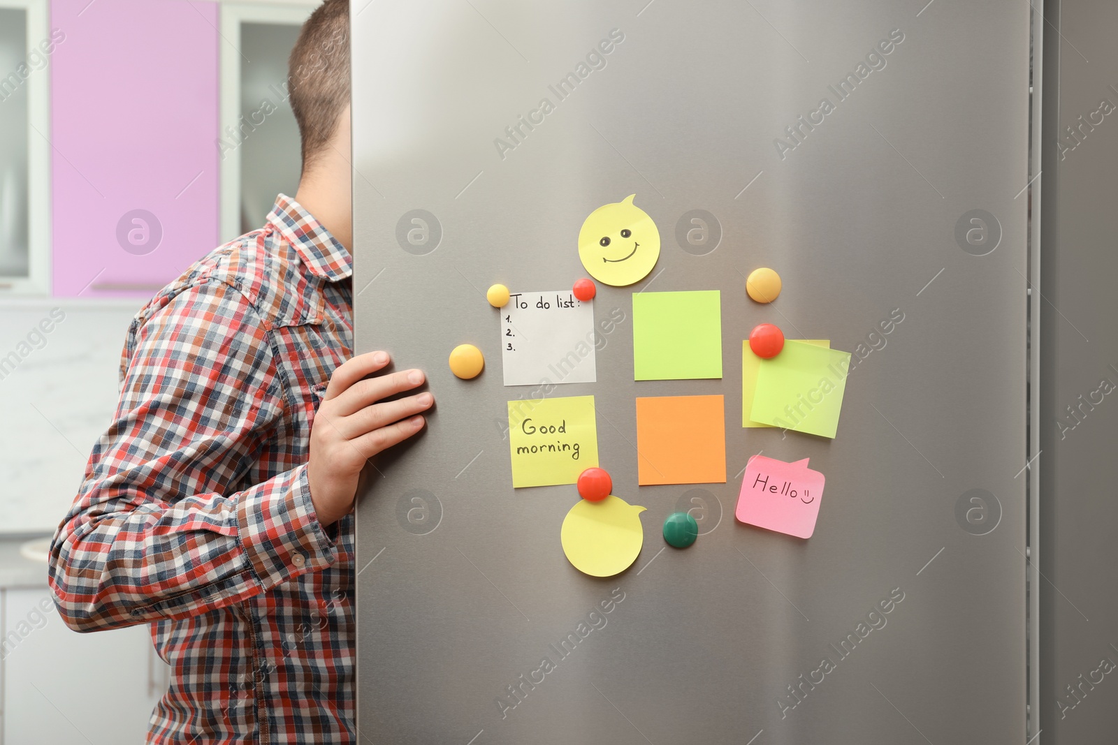 Photo of Man opening refrigerator door with paper sheets and magnets at home, closeup