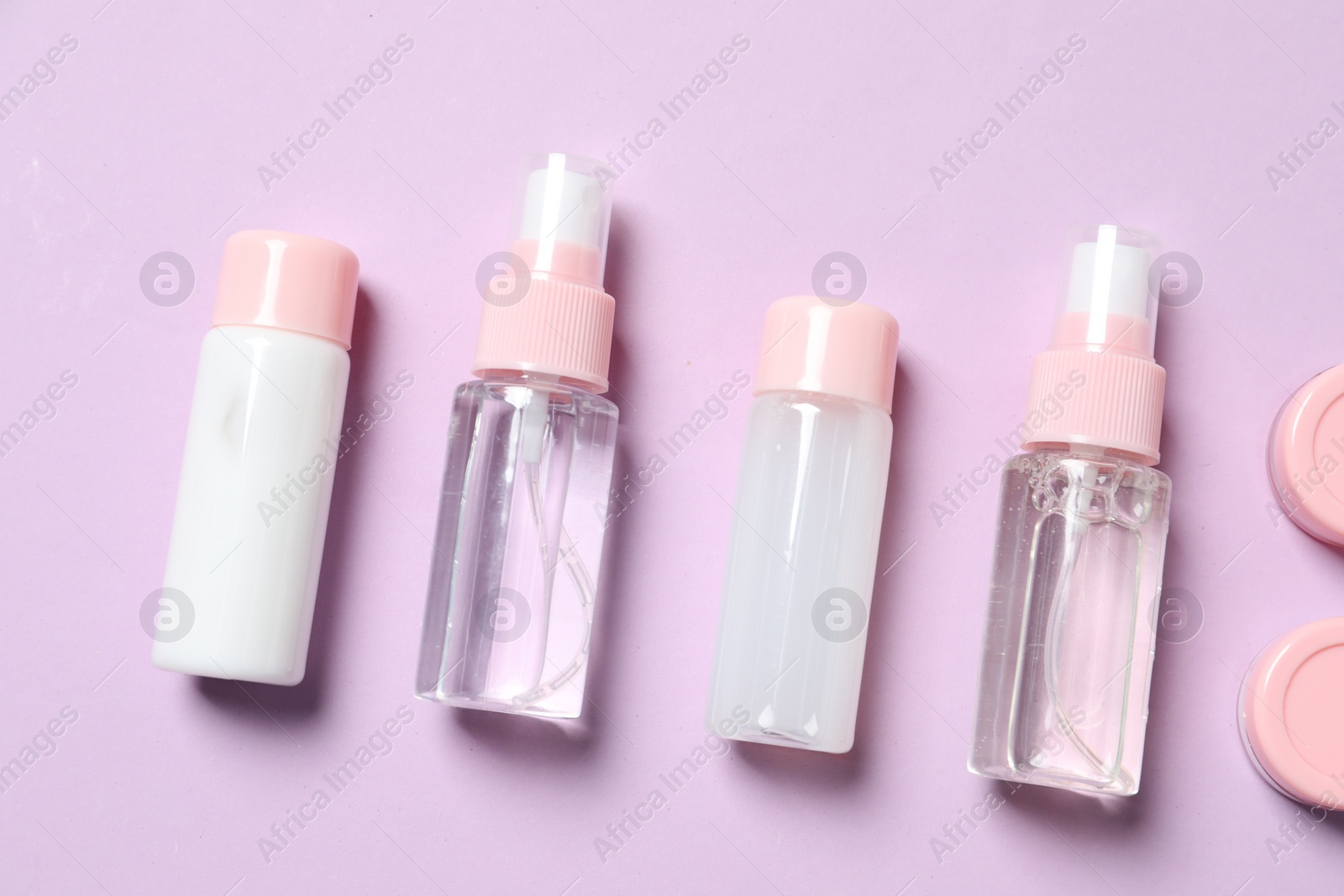 Photo of Cosmetic travel kit. Small containers of personal care products on violet background, flat lay