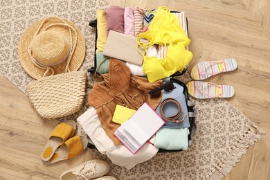 Photo of Open suitcase with clothes, shoes and summer accessories on wooden floor, top view