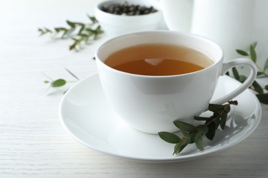 Cup of green tea and eucalyptus leaves on white wooden table