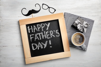 Photo of Flat lay composition with chalkboard, cup of coffee and gift box on wooden background. Father's day celebration