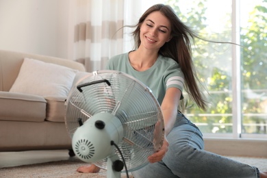 Photo of Woman enjoying air flow from fan on floor in living room. Summer heat