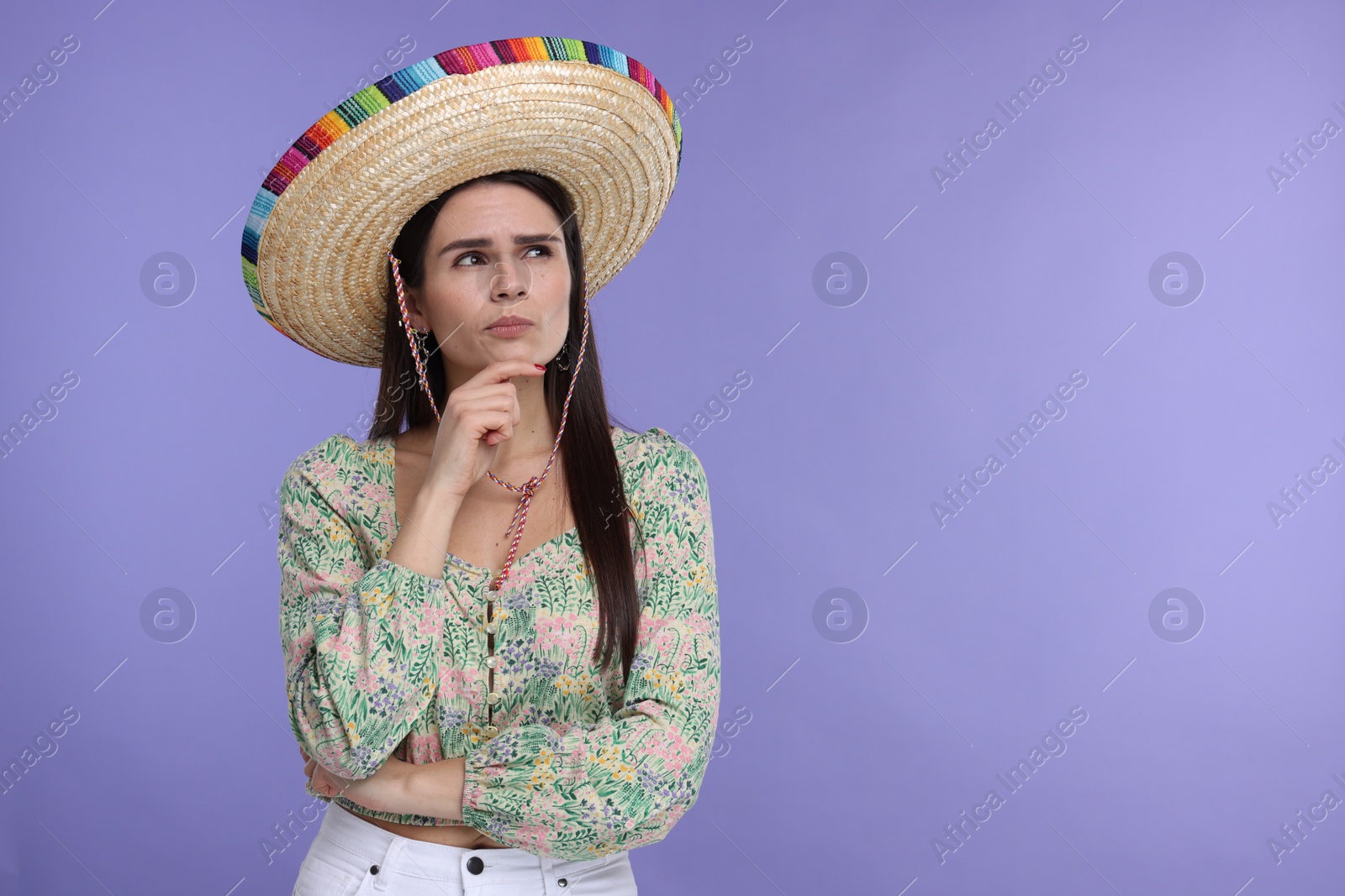 Photo of Thoughtful woman in Mexican sombrero hat on violet background. Space for text