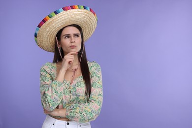 Thoughtful woman in Mexican sombrero hat on violet background. Space for text