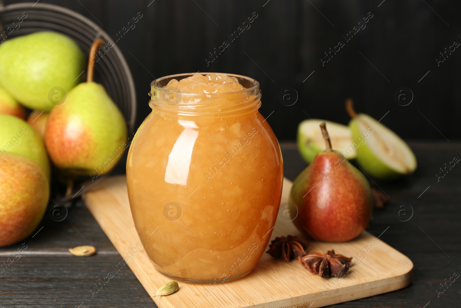 Photo of Delicious pear jam and fresh fruits on black wooden table