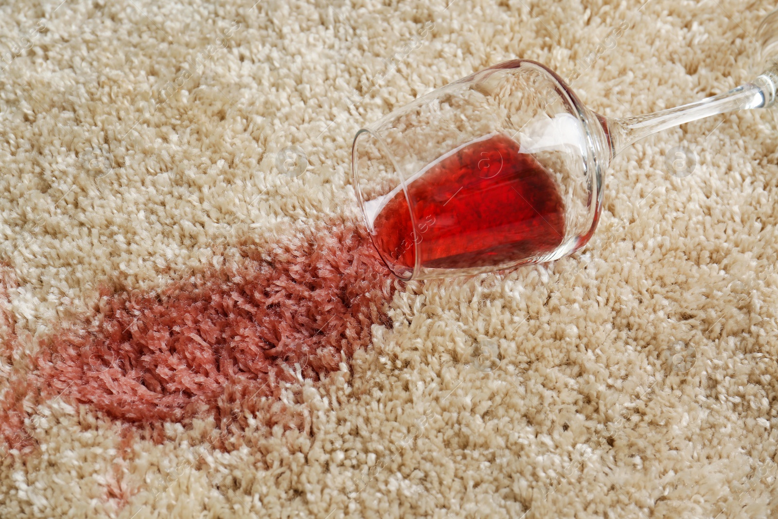 Photo of Overturned glass and spilled red wine on soft carpet, closeup