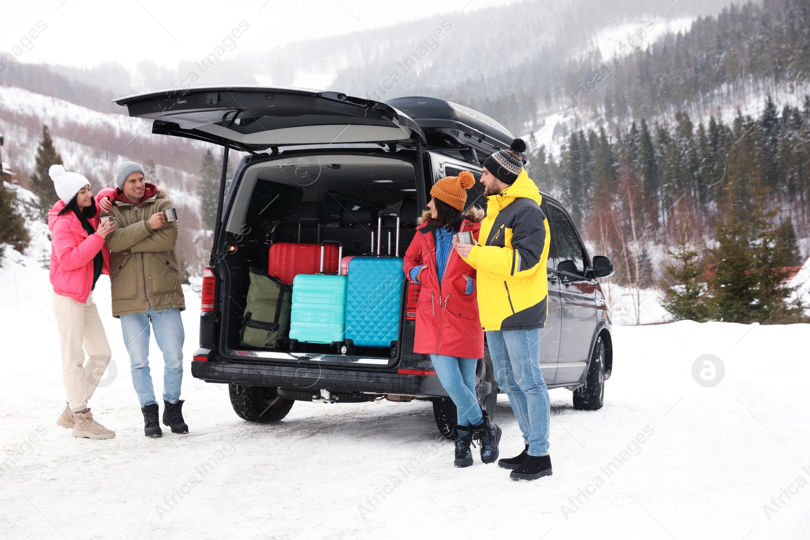 Photo of Group of friends near car with open trunk on snowy road. Winter vacation