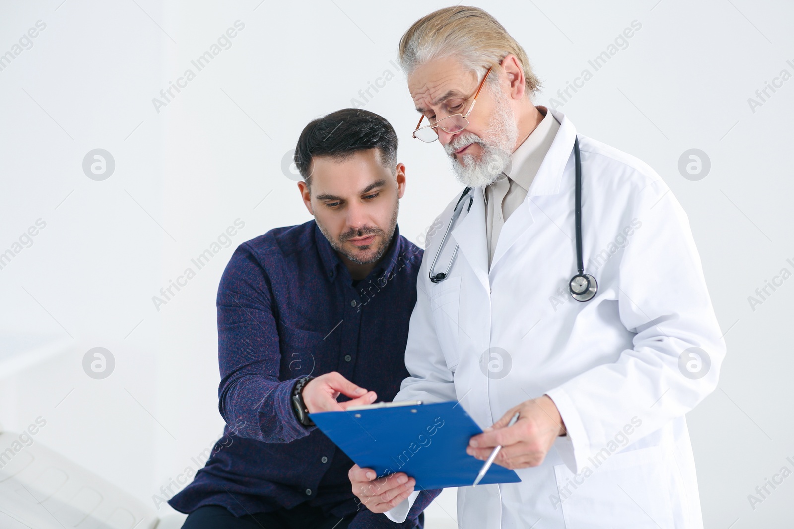 Photo of Senior doctor with clipboard consulting patient in clinic