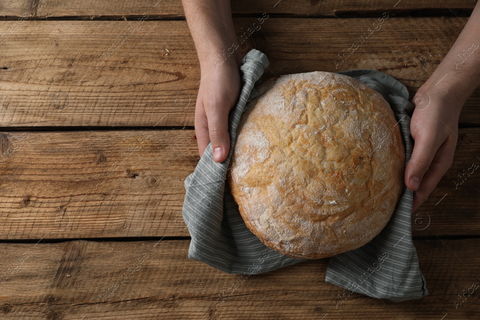 Photo of Man holding loaf of fresh bread at wooden table, top view. Space for text