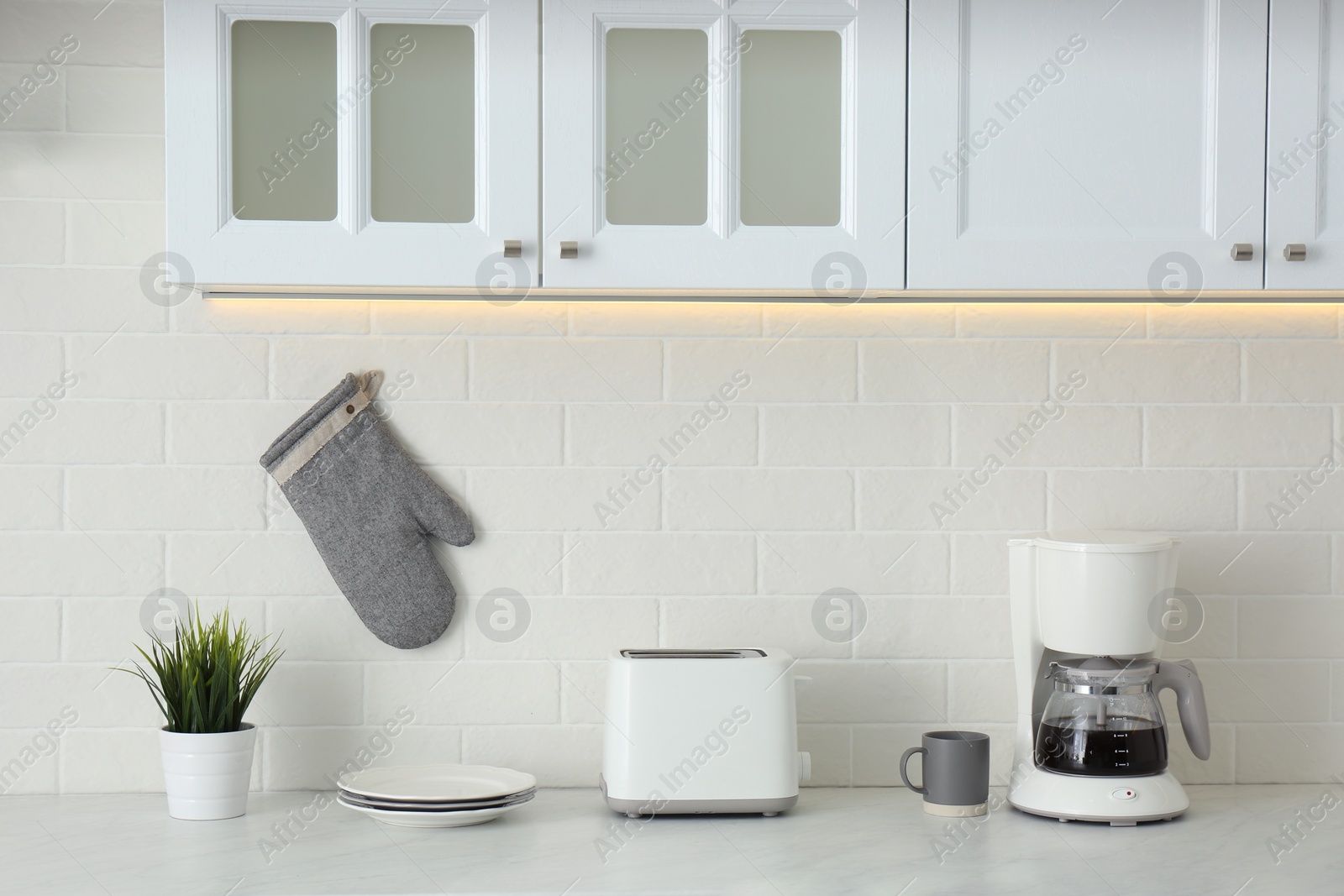 Photo of Modern toaster, coffeemaker and dishware on counter in kitchen