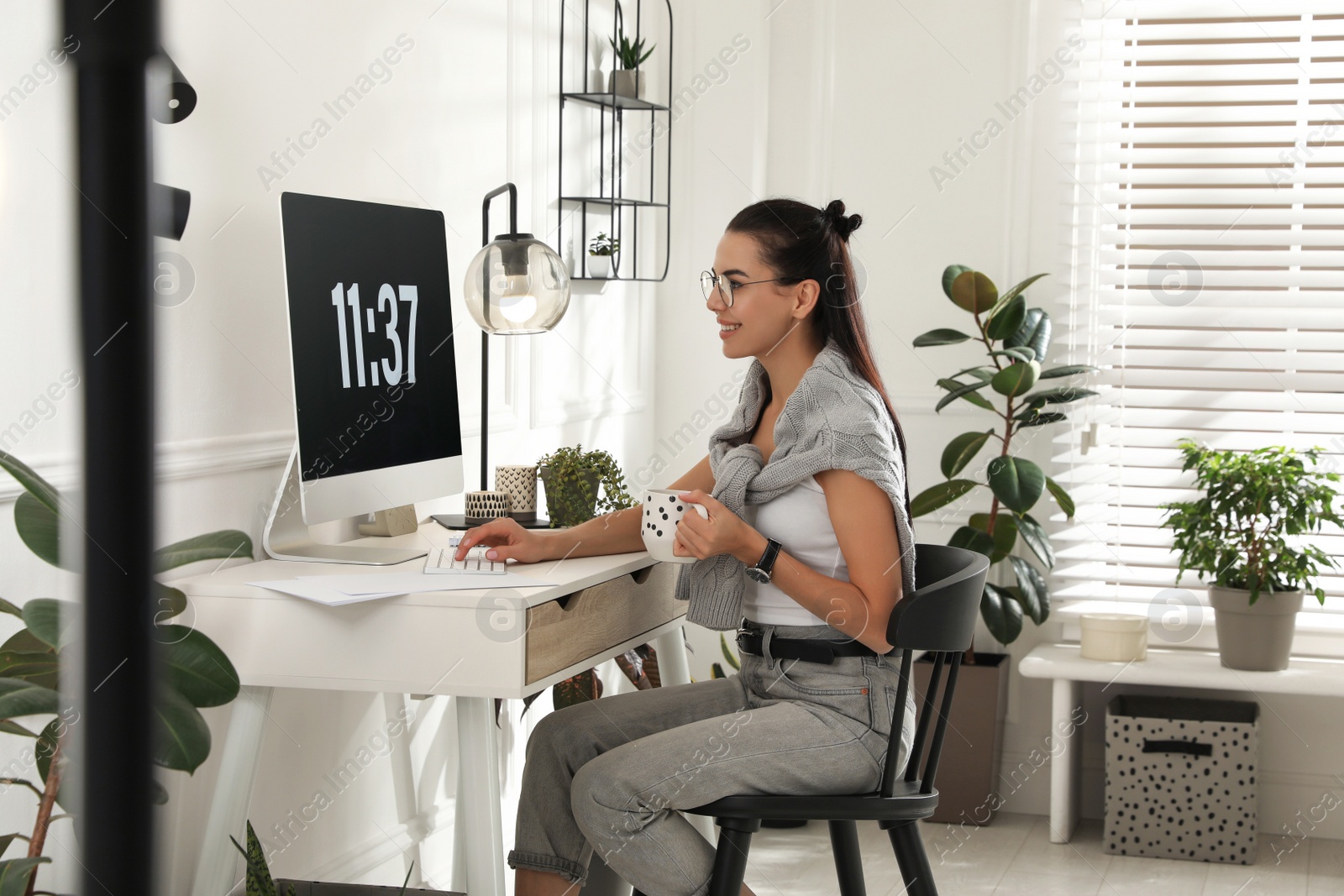 Photo of Young woman with cup of tea working at table in light room. Home office