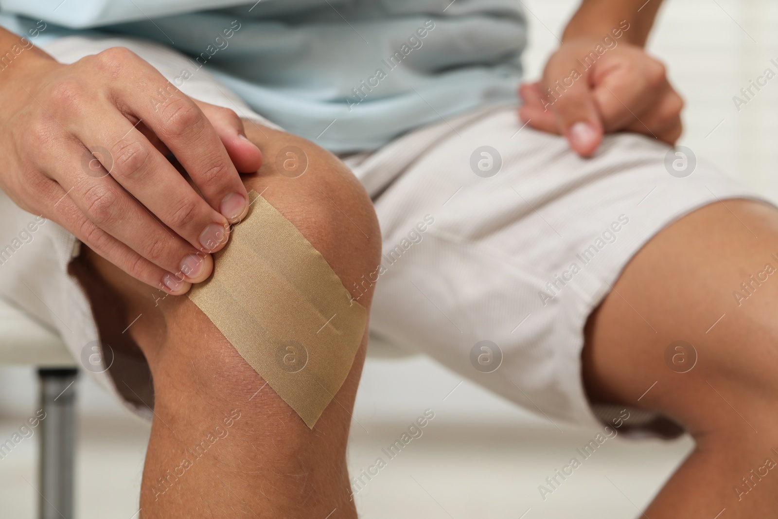 Photo of Man putting sticking plaster onto knee indoors, closeup