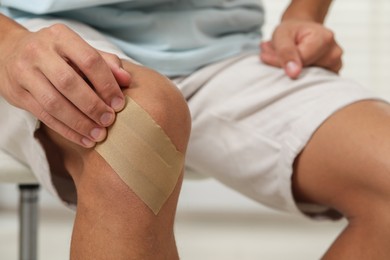 Photo of Man putting sticking plaster onto knee indoors, closeup