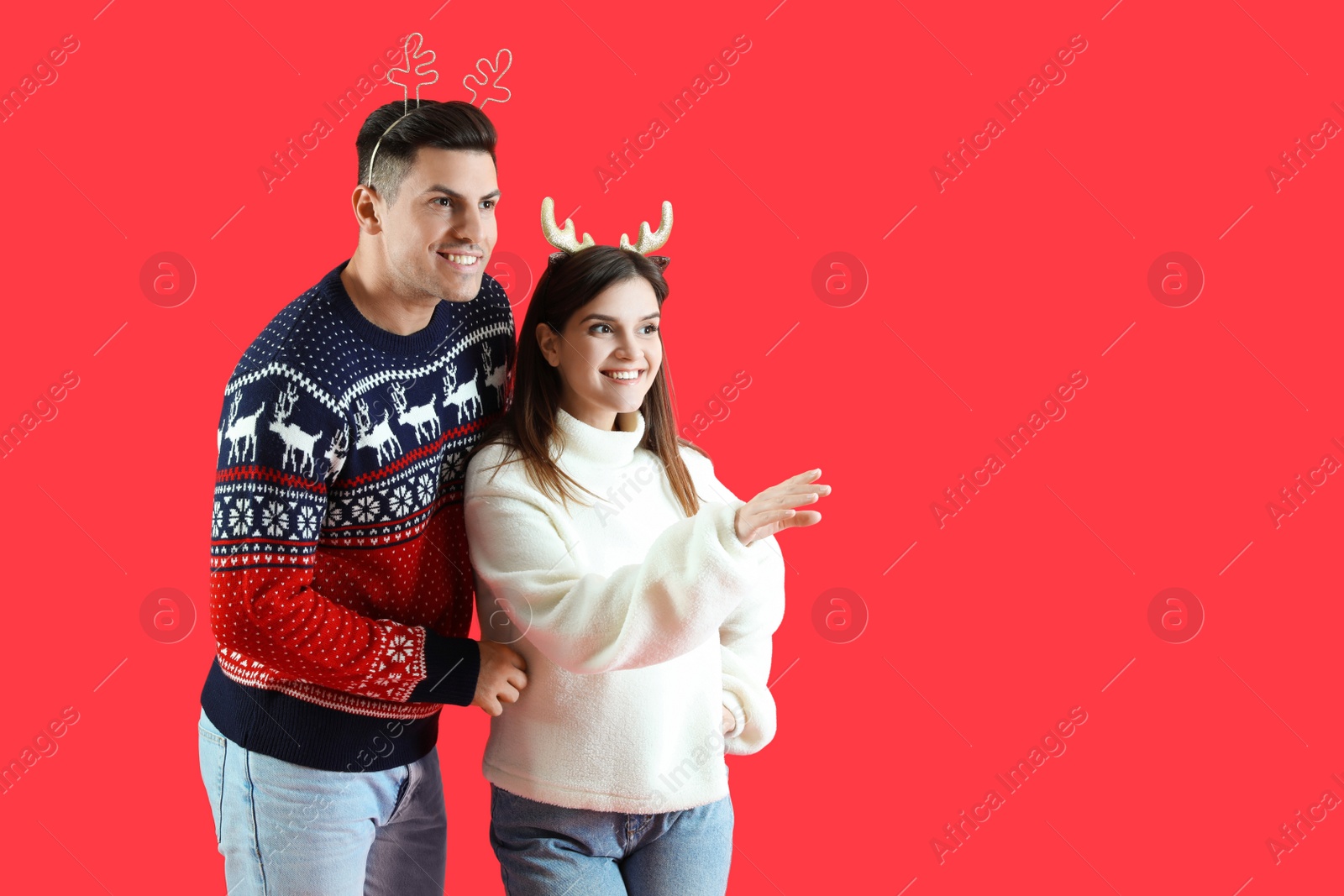 Photo of Beautiful happy couple in Christmas headbands and sweaters on red background. Space for text