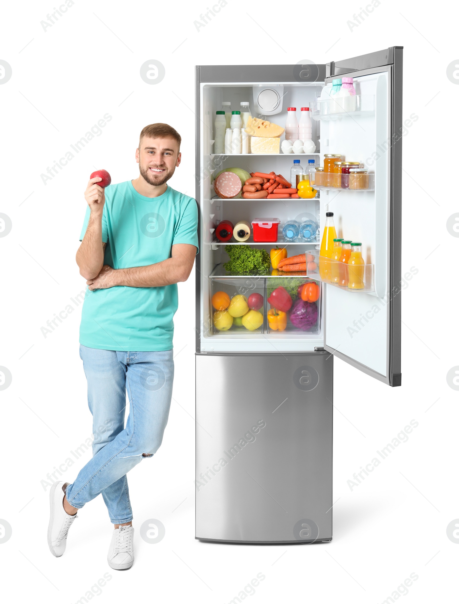 Photo of Young man with apple near open refrigerator on white background