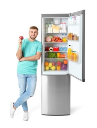 Photo of Young man with apple near open refrigerator on white background