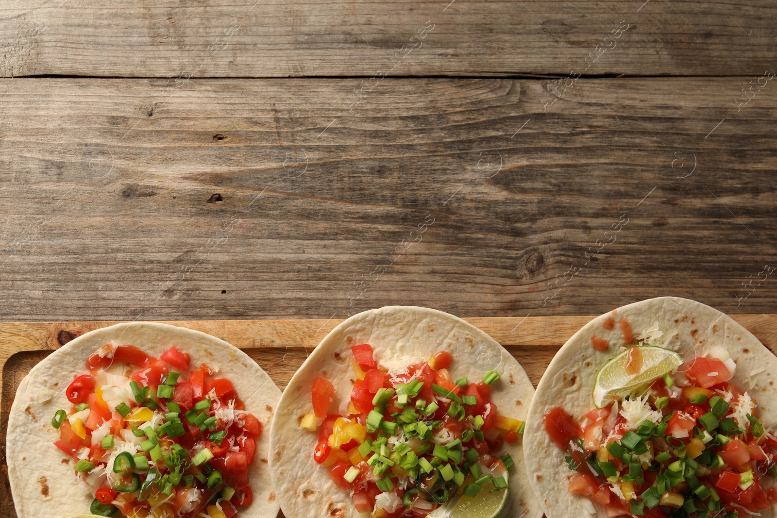 Photo of Delicious tacos with vegetables, green onion, lime and ketchup on wooden table, top view. Space for text